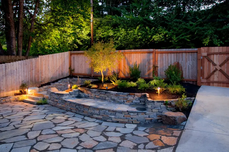 Backyard flagstone patio with lighted curved stone retaining wall