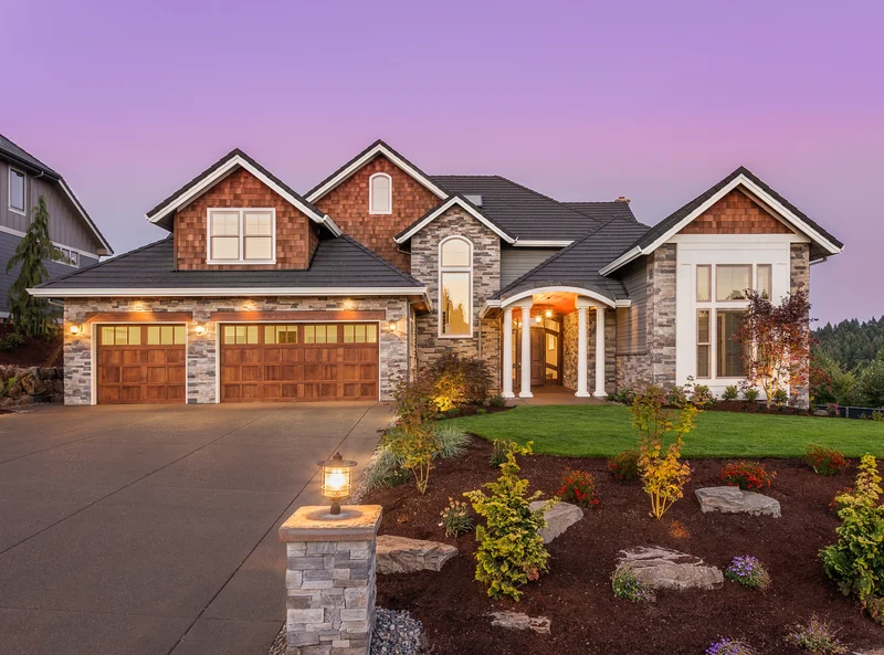 Front yard landscaping with stone mulch beds and a luxury home at dusk