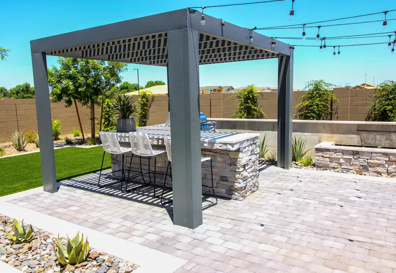 Modern outdoor kitchen under a steel pergola on a paved patio.