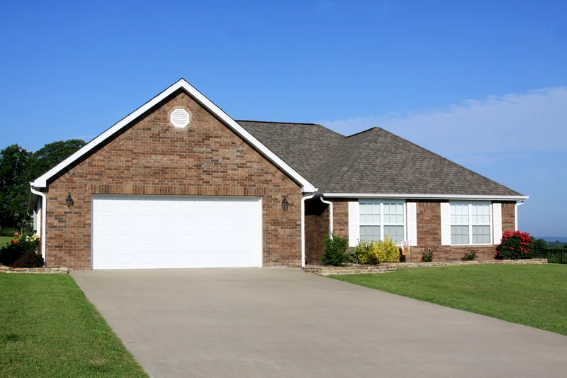 Brick suburban home with a green lawn and concrete driveway.