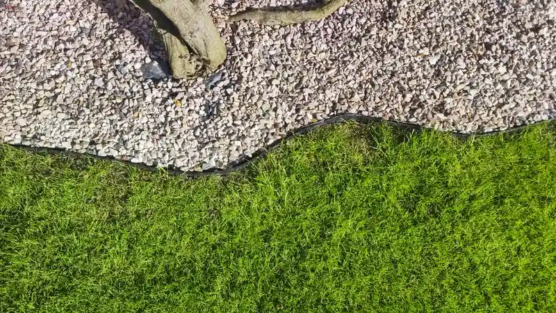 Black garden edging separating green grass and white gravel. Black garden edging separating green grass and white gravel.