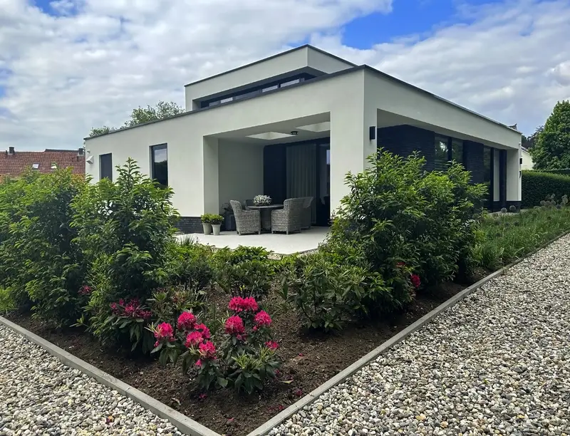 Modern white house with landscaped garden bed featuring pink rhododendrons.